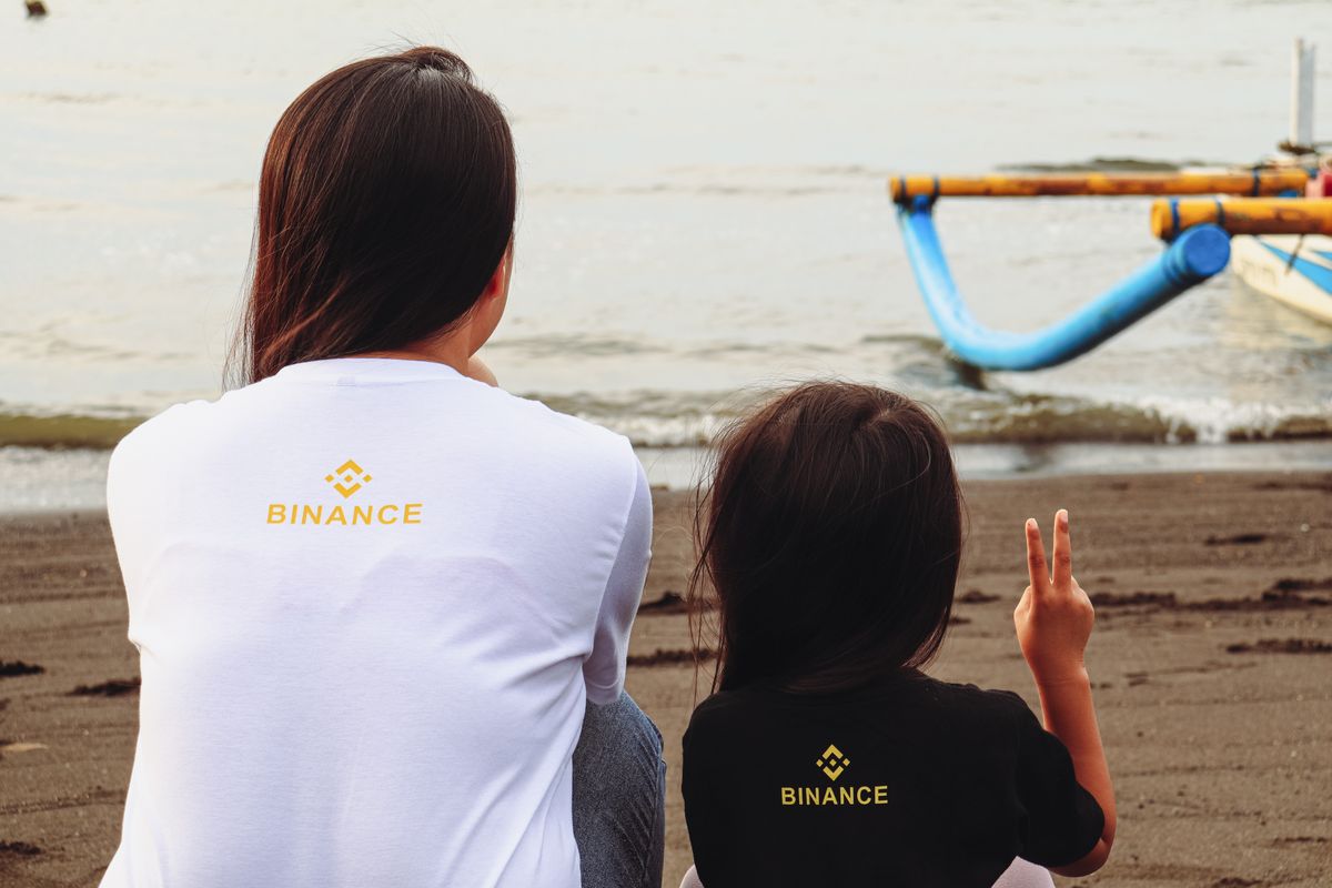 Two people seated on a beach wearing Binance branded t-shirts