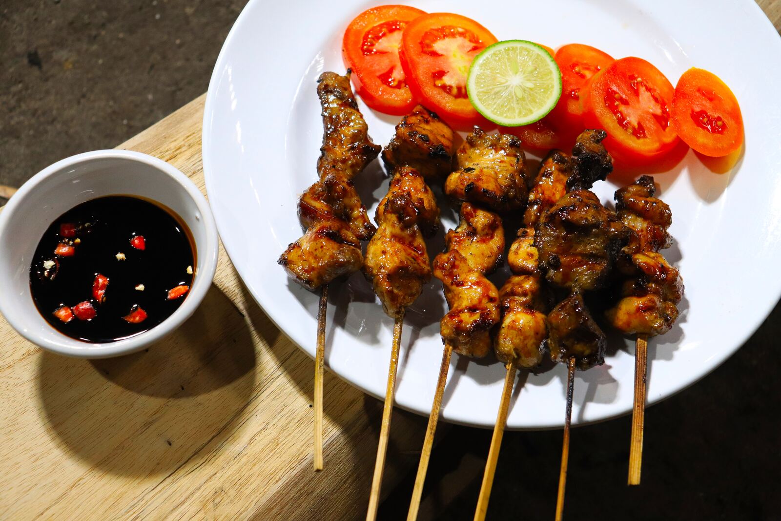 Grilled chicken satay skewers with sweet soy dipping sauce, tomato slices and lime