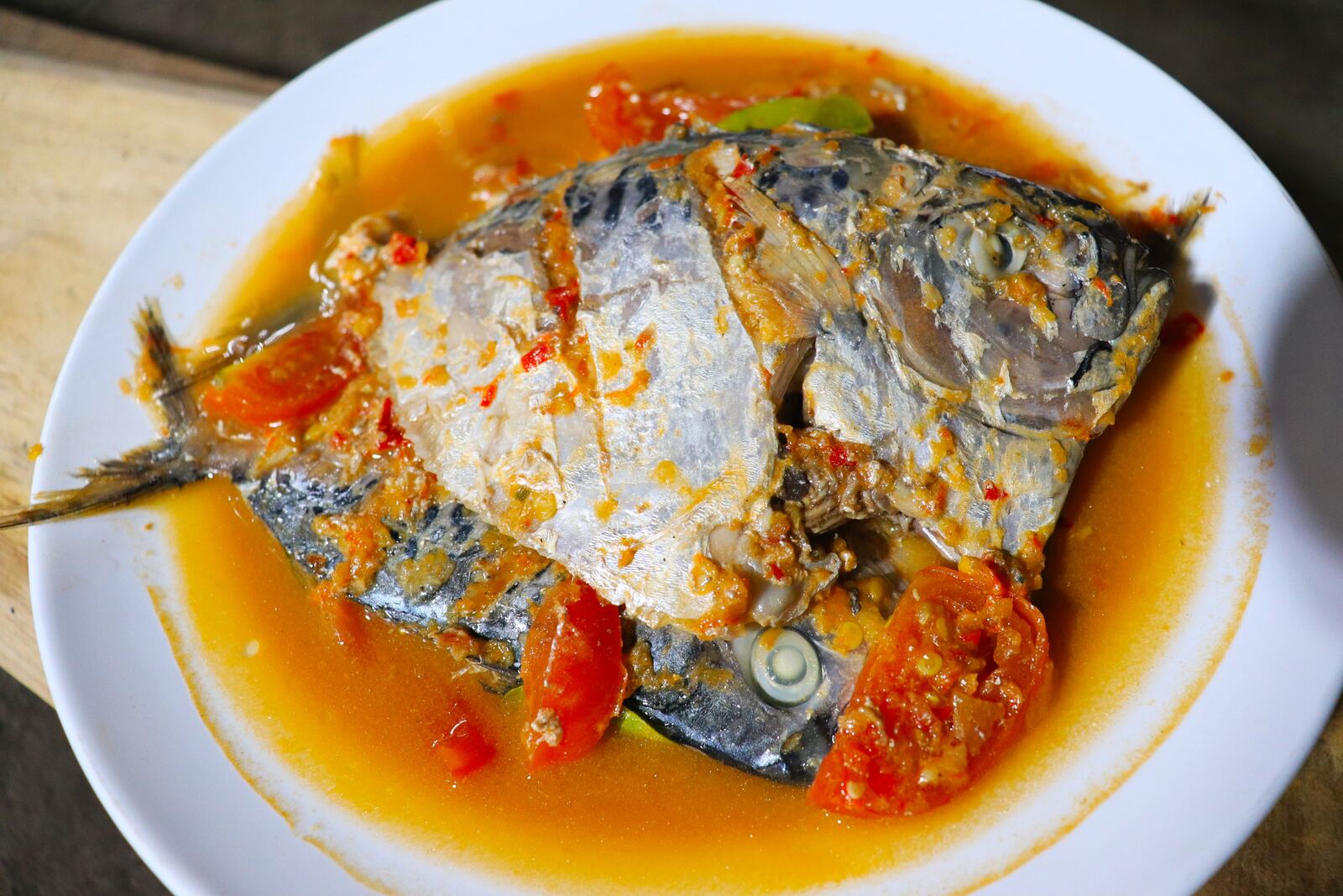 Fish in a spicy tomato and chili sauce on a white plate