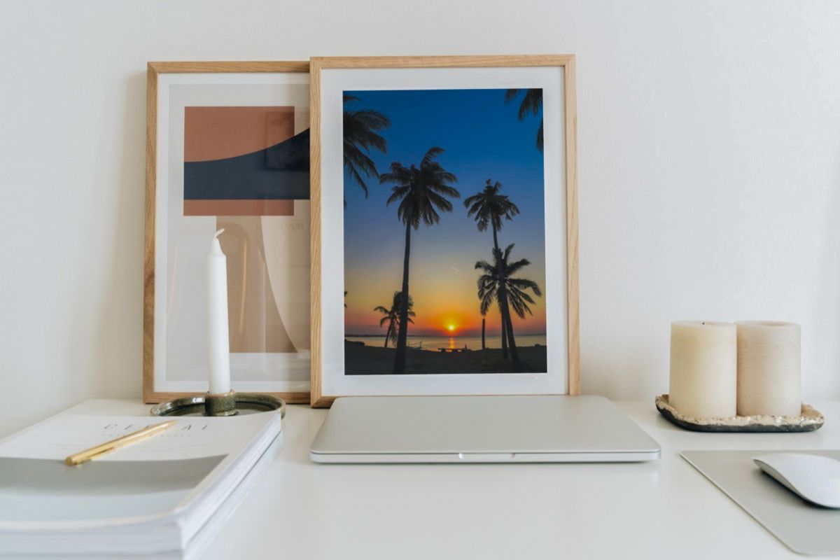 Framed sunset palm tree print on a minimalist desk with laptop and candles